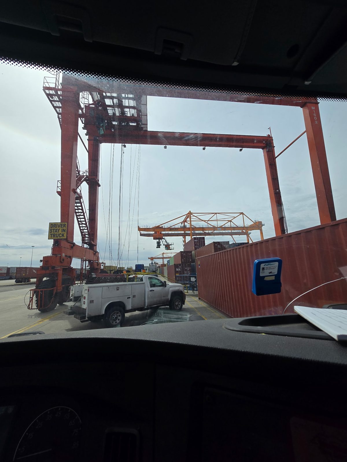 View from a truck cab toward a gantry crane at a rail ramp